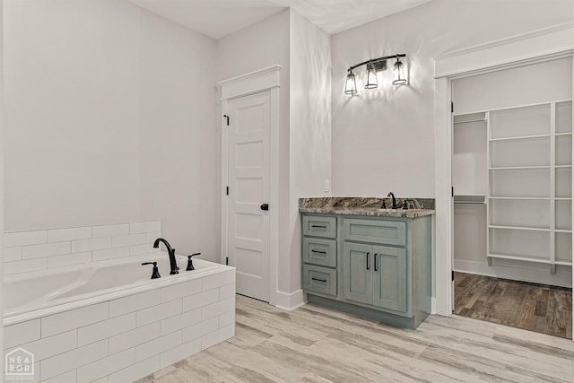 bathroom featuring a bath, a walk in closet, vanity, and wood finished floors
