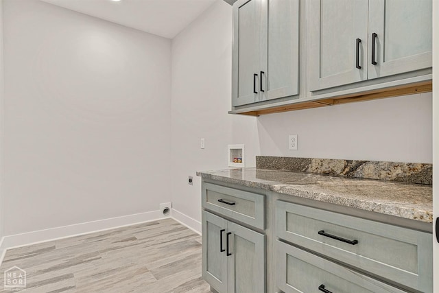 clothes washing area featuring hookup for an electric dryer, baseboards, washer hookup, light wood-style floors, and cabinet space