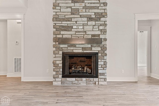interior details featuring visible vents, a stone fireplace, wood finished floors, and baseboards
