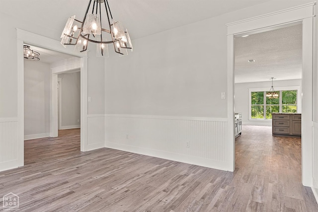 unfurnished dining area with a wainscoted wall, a notable chandelier, wood finished floors, and a textured ceiling