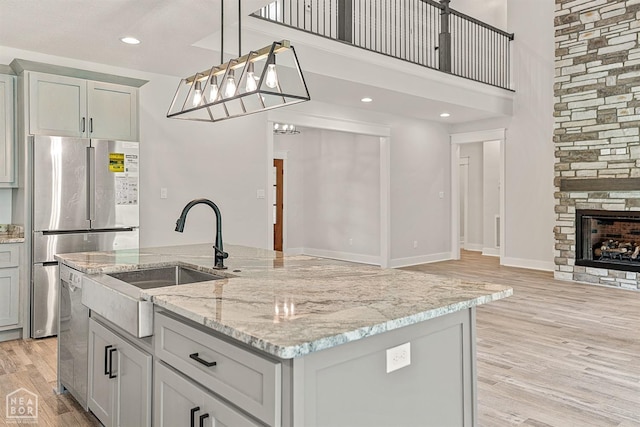 kitchen featuring light wood-style flooring, dishwasher, a sink, open floor plan, and a center island with sink