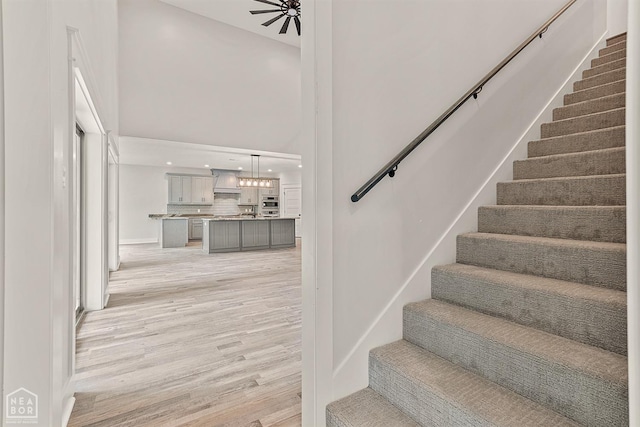 stairs featuring recessed lighting, a towering ceiling, an inviting chandelier, and wood finished floors