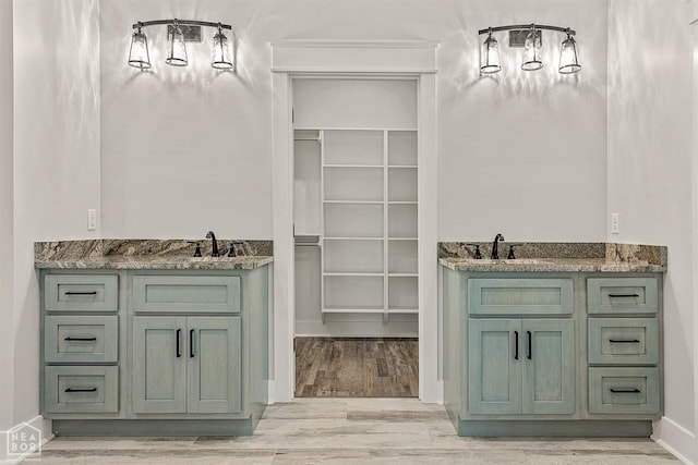 full bathroom featuring a sink, two vanities, a walk in closet, and wood finished floors