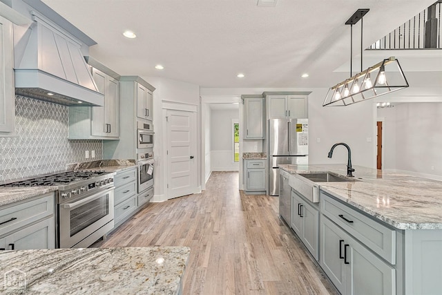 kitchen with a sink, appliances with stainless steel finishes, custom range hood, and gray cabinetry