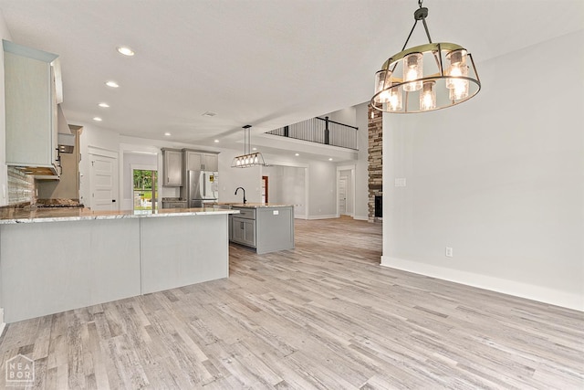 kitchen featuring light wood-style floors, freestanding refrigerator, an inviting chandelier, a peninsula, and gray cabinetry
