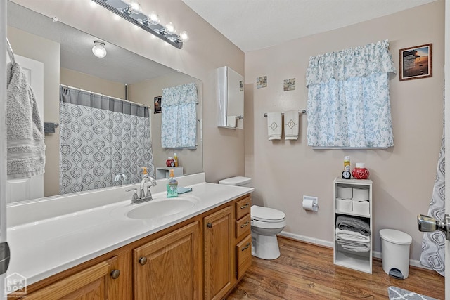 bathroom with baseboards, a shower with curtain, toilet, vanity, and wood finished floors