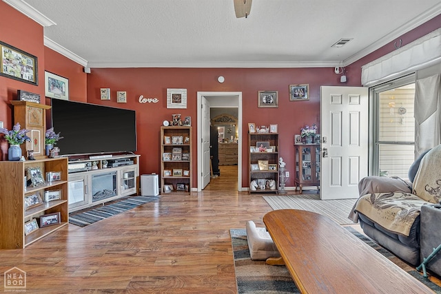 living area with baseboards, a textured ceiling, crown molding, visible vents, and wood finished floors