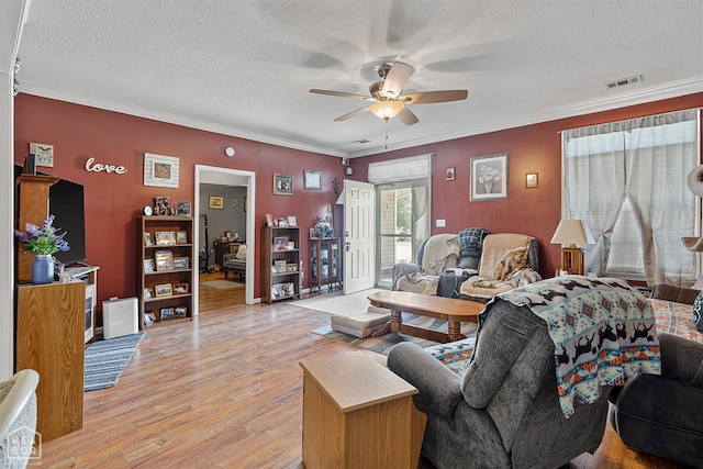 living room with light wood finished floors, visible vents, a ceiling fan, and ornamental molding