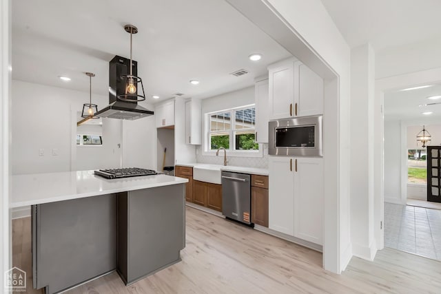 kitchen with appliances with stainless steel finishes, a sink, range hood, backsplash, and visible vents
