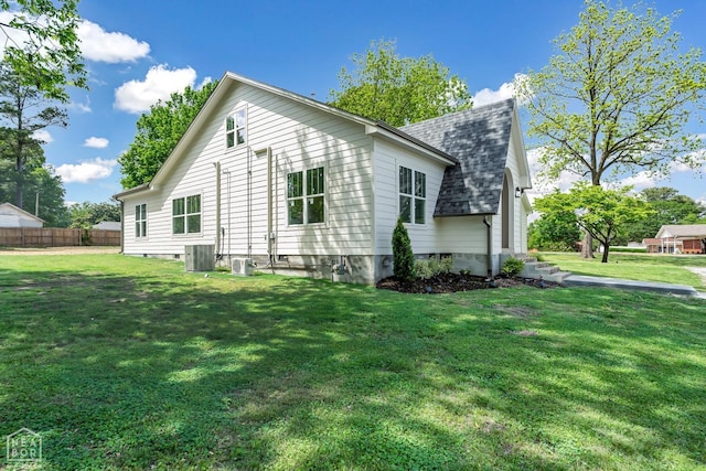exterior space with roof with shingles, fence, central AC unit, and a yard