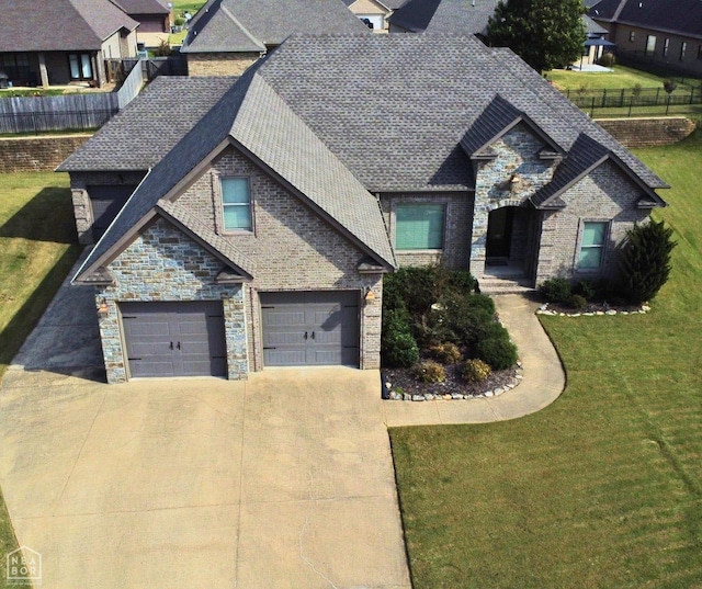view of front of property with stone siding, a garage, fence, a front lawn, and driveway