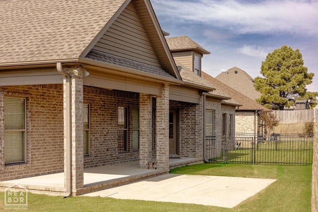 rear view of property featuring a lawn, fence, a patio, brick siding, and roof with shingles