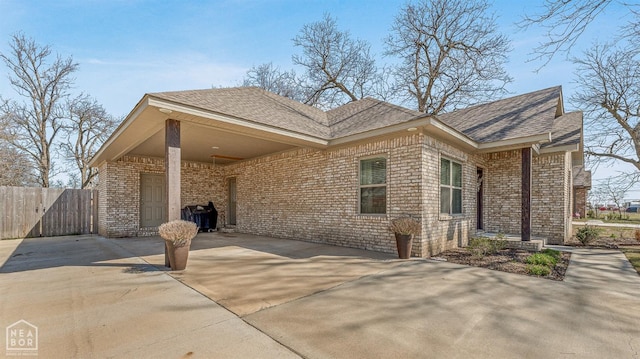 view of property exterior featuring concrete driveway, roof with shingles, an attached carport, brick siding, and fence