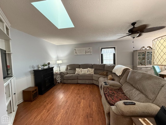 living room with a wainscoted wall, a textured ceiling, a skylight, wood finished floors, and ceiling fan
