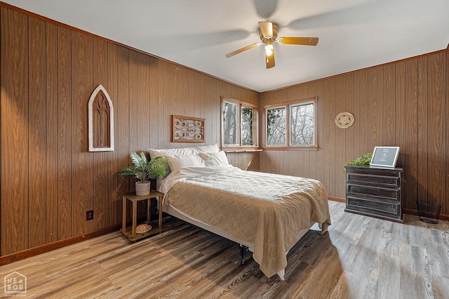 bedroom with baseboards, ceiling fan, wood walls, and wood finished floors