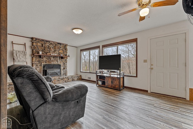 living room with a fireplace, a textured ceiling, a ceiling fan, baseboards, and wood finished floors