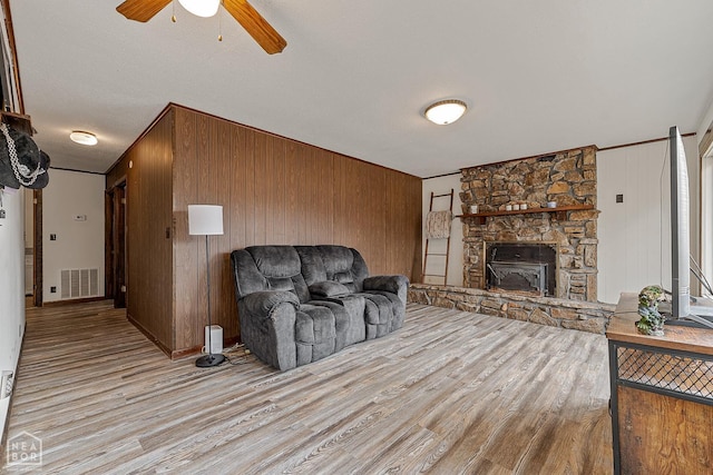 living room featuring a ceiling fan, wood walls, light wood-style flooring, and visible vents