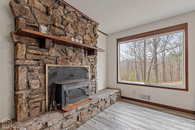 unfurnished living room featuring a textured ceiling, visible vents, a fireplace, wood finished floors, and baseboards