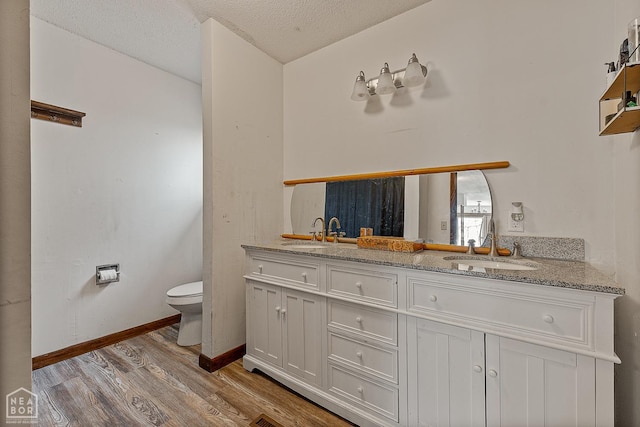 bathroom featuring double vanity, toilet, a sink, and wood finished floors