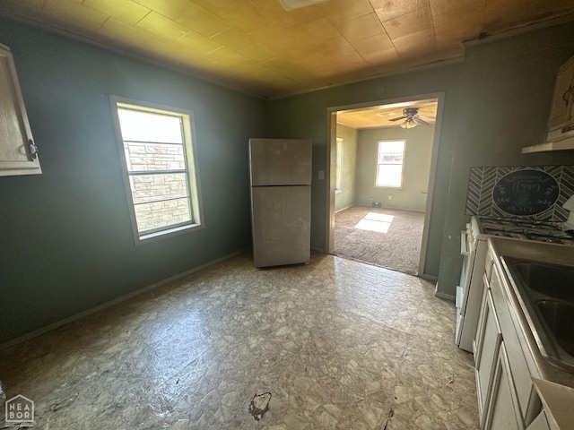 kitchen featuring ceiling fan, baseboards, freestanding refrigerator, white range with gas cooktop, and under cabinet range hood