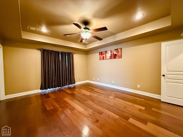 spare room with baseboards, a ceiling fan, visible vents, a raised ceiling, and wood finished floors