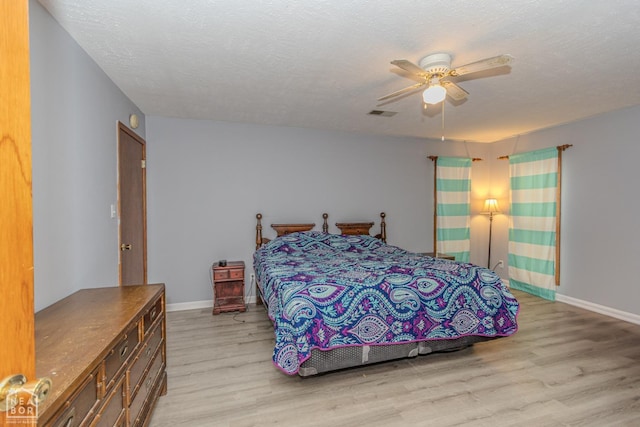 bedroom featuring ceiling fan, a textured ceiling, light wood-style flooring, baseboards, and visible vents
