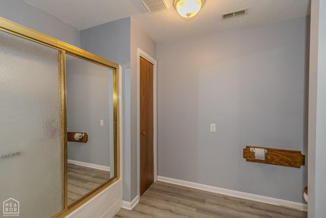 full bathroom featuring baseboards, a shower with door, wood finished floors, and visible vents