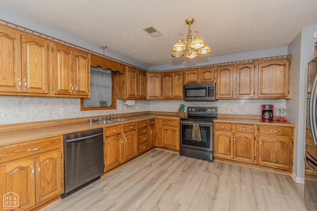 kitchen with visible vents, appliances with stainless steel finishes, brown cabinets, a sink, and an inviting chandelier