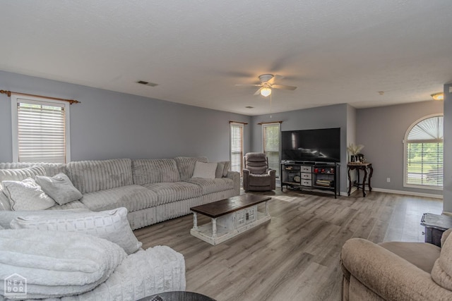 living room featuring ceiling fan, visible vents, plenty of natural light, and wood finished floors