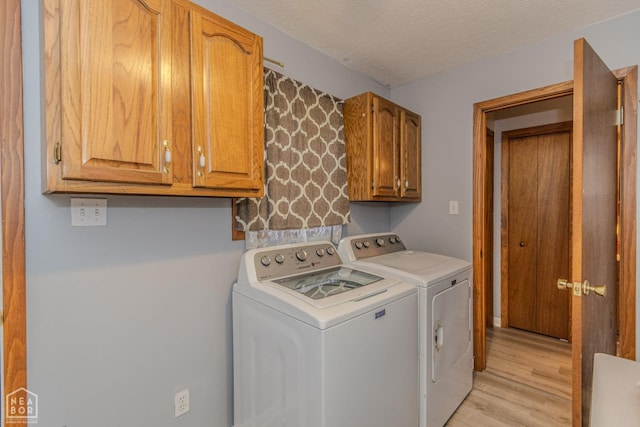 laundry room featuring washing machine and clothes dryer, a textured ceiling, light wood-style flooring, and cabinet space