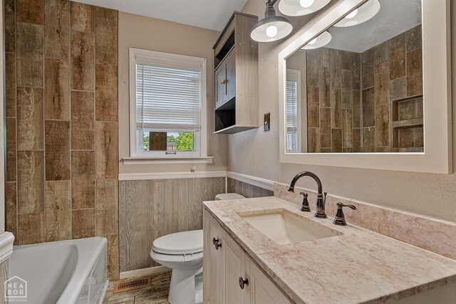 bathroom with toilet, a tub to relax in, wainscoting, and vanity