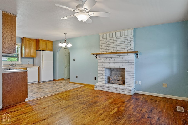 kitchen with white appliances, ceiling fan, a fireplace, light wood-type flooring, and baseboards