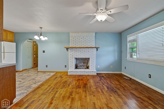 unfurnished living room featuring wood finished floors, arched walkways, a ceiling fan, a brick fireplace, and a chandelier