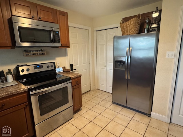 900 Sycamore Cv, Jonesboro, AR 72404 - kitchen with stainless steel appliances, dark countertops, light tile patterned floors, and brown cabinets