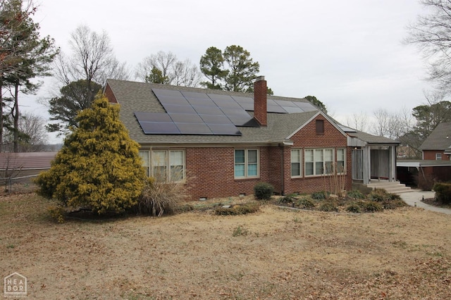 rear view of house featuring roof with shingles, a chimney, solar panels, and brick siding