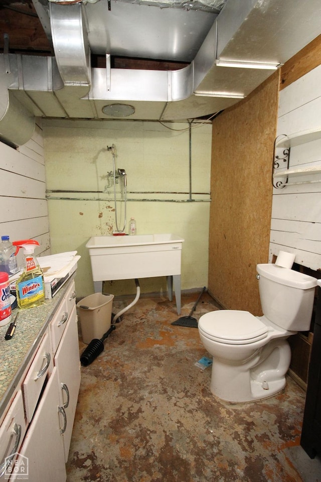 bathroom with toilet, wood walls, and unfinished concrete flooring