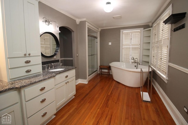 bathroom with crown molding, a shower stall, a freestanding tub, vanity, and wood finished floors