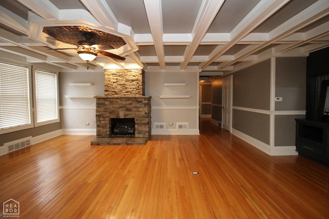 unfurnished living room with a ceiling fan, wood finished floors, a stone fireplace, and visible vents