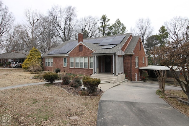 view of front of house featuring brick siding, roof mounted solar panels, driveway, and a chimney