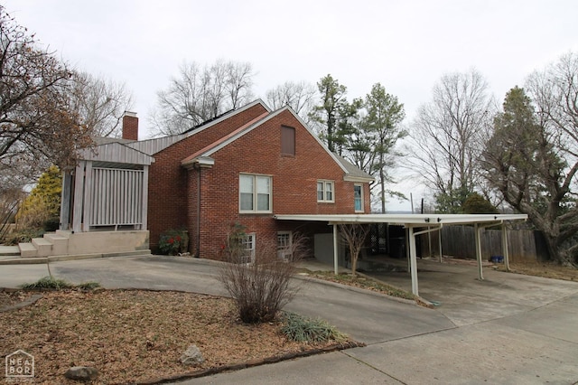 view of side of property with a carport, a chimney, concrete driveway, and brick siding