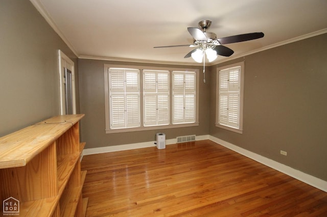 empty room with ornamental molding, baseboards, a ceiling fan, and visible vents