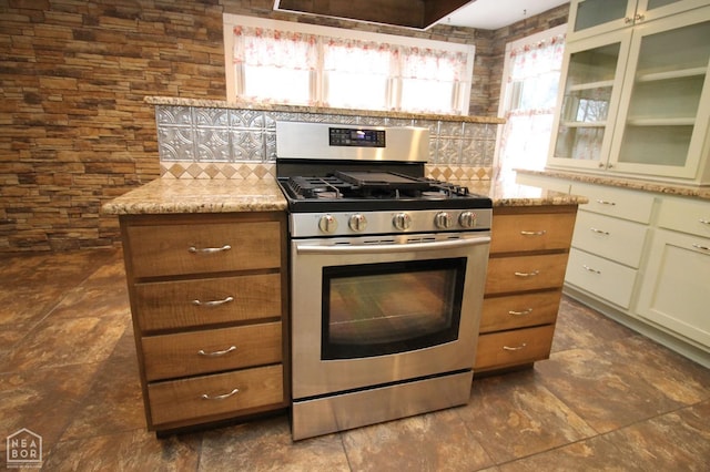 kitchen featuring tasteful backsplash, light stone countertops, glass insert cabinets, and gas stove