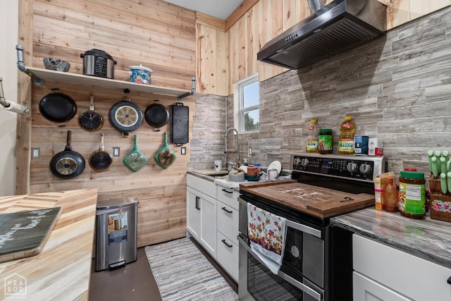 kitchen with wall chimney range hood, white cabinets, a sink, wooden counters, and range with two ovens