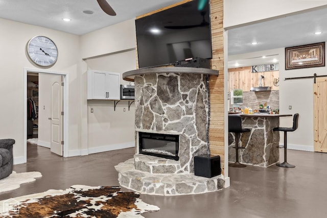 living area featuring ceiling fan, a stone fireplace, recessed lighting, a barn door, and baseboards