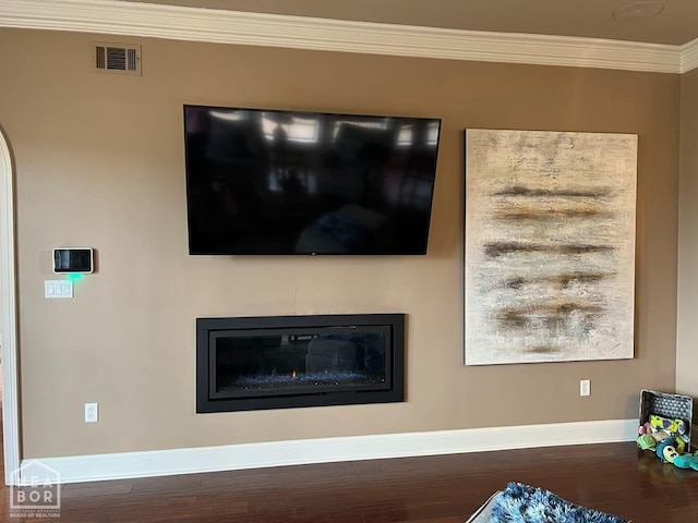 room details featuring a glass covered fireplace, ornamental molding, visible vents, wood finished floors, and baseboards