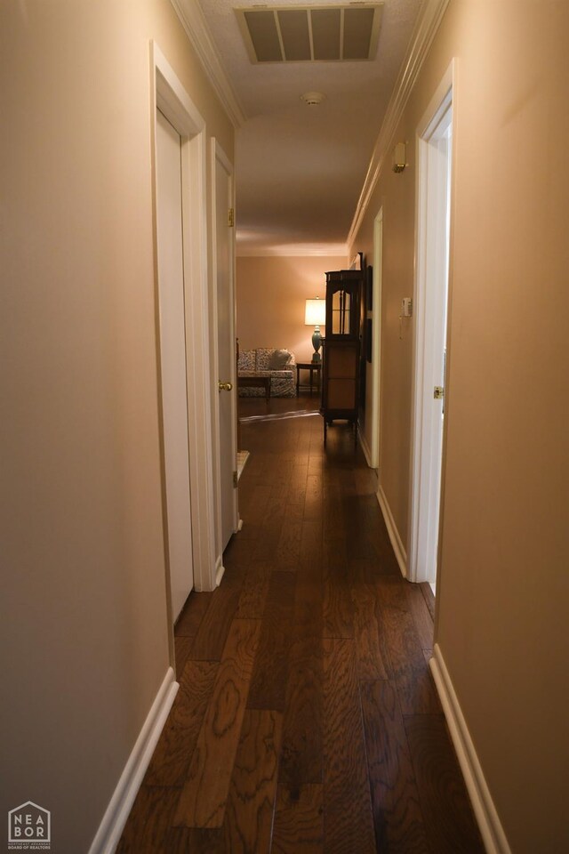 hall with visible vents, baseboards, crown molding, and dark wood finished floors