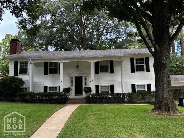 bi-level home featuring a porch, a chimney, and a front yard