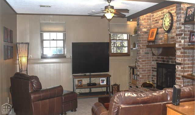 carpeted living area with ornamental molding, a ceiling fan, wainscoting, and a brick fireplace