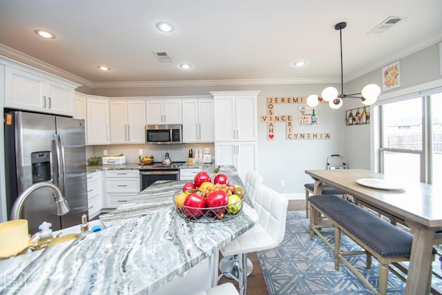 kitchen featuring crown molding, visible vents, a breakfast bar, white cabinets, and stainless steel appliances