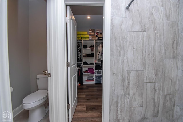 bathroom with walk in shower, baseboards, a spacious closet, toilet, and wood finished floors